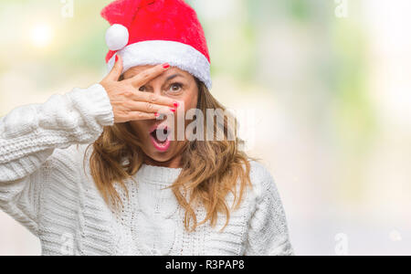 Mittleres Alter senior Hispanic Frau tragen Mütze über isolierte Hintergrund peeking im Schock für Gesicht und Augen mit der Hand, durch Fin suchen Stockfoto