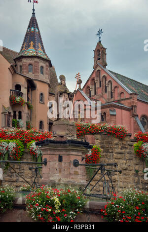 Die Europäische Union, Frankreich, Elsass, Eguisheim Dorf. St Leon Kirche und Brunnen auf der Place du chateau Platz in mittelalterlichen Eguisheim Dorf auf der Weinstraße. Stockfoto