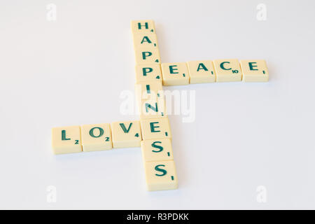 Scrabble-Spiel Buchstabensteine mit Score Wert bilden die Worte Frieden, Liebe und Glück auf weißem Hintergrund. Stockfoto