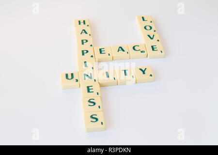 Scrabble-Spiel Buchstabensteine mit Score Wert bilden die Worte Frieden, Liebe, Einheit und Glück auf weißem Hintergrund. Stockfoto
