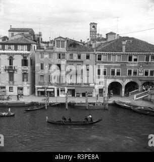 1950 s, historischen, einen Blick auf einen Kanal und Gebäuden in Venedig, einschließlich einer Gondel auf dem Wasser, das traditionelle Symbol der italienischen Stadt. Die Hauptstadt der Region Venetien ist auf eine Gruppe von 118 kleine Inseln, die durch Kanäle getrennt und durch mehr als 400 Brücken miteinander verbunden sind. Stockfoto