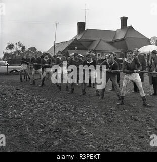 1965, Tauziehen Wettbewerb, ein Team von männlichen Rugby Spieler außerhalb der Veranstaltung in ein schlammiges Feld, England, UK. Stockfoto