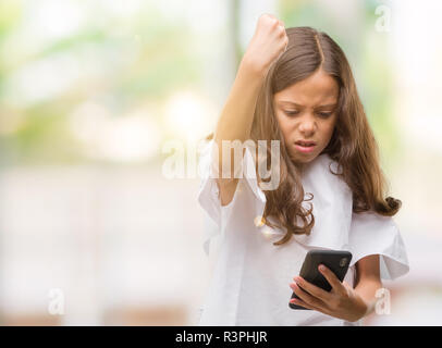 Brunette Hispanic Mädchen mit Smartphone genervt und frustriert schrie mit Zorn, verrückt und schreien mit erhobener Hand, Wut Konzept Stockfoto