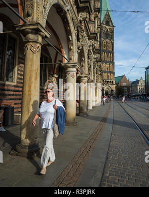 Marktplatz, Bremen. Deutschland. Deutschland. Ein Blick vom Rathaus auf den Marktplatz. Unter den Arkaden des Rathauses, Rathaus fotografiert, mit der Menschen vorbei. Es ist eine helle, sonnige Nachmittag und die starke Sonneneinstrahlung ist Casting starke Schatten Drama, um die Szene hinzuzufügen. Stockfoto