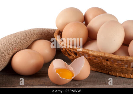 Eier auf einem hölzernen Tisch in einem Weidenkorb auf weißem Hintergrund Stockfoto