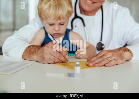 Kind sitzt auf dem Schoß, während der Arzt ausfüllen Immunisierung Karte Stockfoto