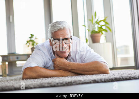 Lächelnd reifer Mann entspannende liegen auf dem Teppich zu Hause Stockfoto