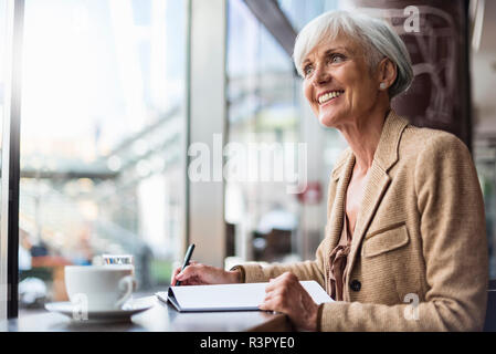 Lächelnd senior Geschäftsfrau Notizen in einem Cafe Stockfoto