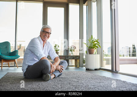 Lächelnd reifer Mann entspannten Sitzen auf dem Teppich zu Hause Stockfoto