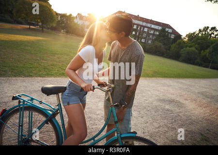 Junge Frau mit Fahrrad, küsste ihren Freund im Park Stockfoto