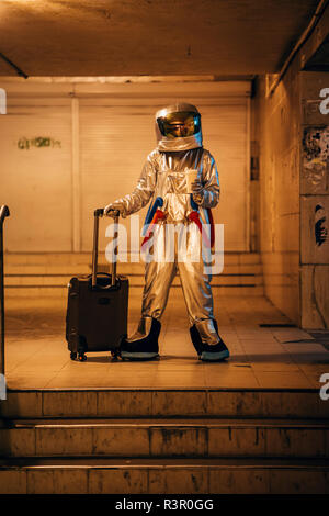 Spaceman in der Stadt in der Nacht stehend in Unterführung mit rollenden Koffer und Kaffee zum Mitnehmen Stockfoto