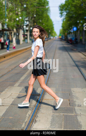 Junge Frau beim Überqueren einer Straße mit Straßenbahngleise in der Stadt Stockfoto