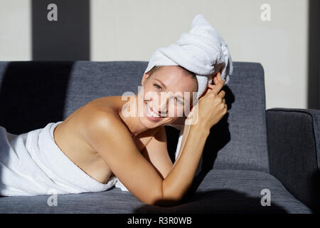 Portrait von lächelnden Frau in ein Handtuch eingewickelt auf der Couch liegen Stockfoto