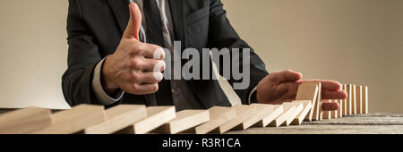 In der breiten Ansicht Bild der Geschäftsmann mit Daumen nach oben unterzeichnen, als er die Dominos fallen mit seiner Hand in einem konzeptionellen Bild unterbrochen wird. Stockfoto