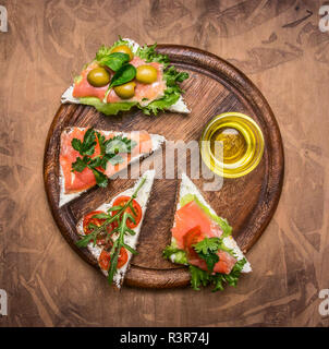 Appetitliche Sandwiches mit gesalzener roten Fisch zum Mittagessen, Cherry Tomaten, Rucola, Quark und Kräuter, auf einer kreisförmigen Schneidbrett gesäumt, Ansicht von oben Stockfoto