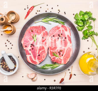 Zwei saftiges rohes Schweinefleisch Steaks mit Rosmarin und andere Gewürze, die in einer Pfanne Pfanne gelegt, um den ausgelegten Zutaten, die Ansicht von oben Stockfoto