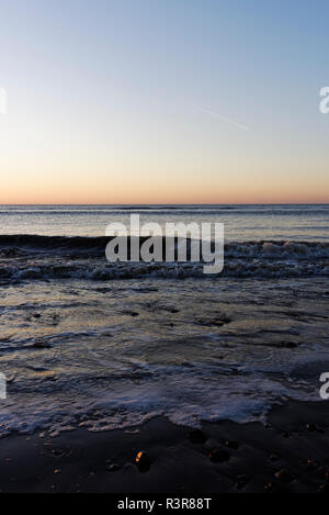 Wellen nähern sich bei Ebbe dem Meer und rotes Licht am Horizont, Sonnenuntergang an der Küste in cleveleys an der fylde-Küste in lancashire uk Stockfoto