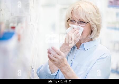 Kranken älteren Frau liest Label auf Pille Flasche in der Apotheke während blasen Nase. Stockfoto