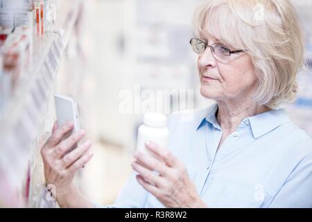 Ältere Frau Prüfung Medizin auf Mobiltelefon in der Apotheke. Stockfoto