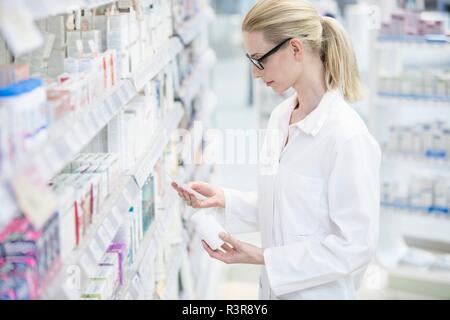 Weibliche Apotheker lesen Rezept mit Pille Flasche in der einen Hand in der Apotheke. Stockfoto