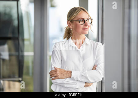 Im Amt lehnte sich gegen Fenster Geschäftsfrau, mit verschränkten Armen Stockfoto