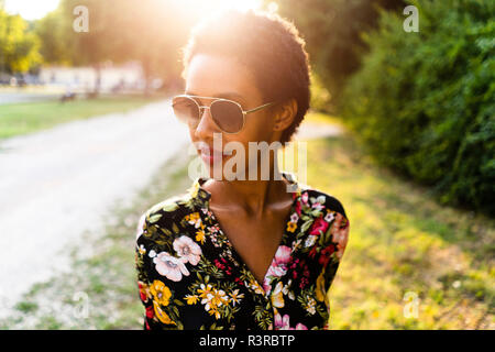 Modische junge Frau mit Sonnenbrille im Freien bei Sonnenuntergang Stockfoto