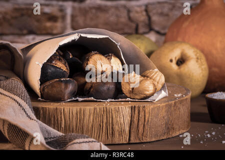 Gebratene Kastanien in einer Papiermembran, auf eine rustikale Küche Arbeitsplatte. Stockfoto