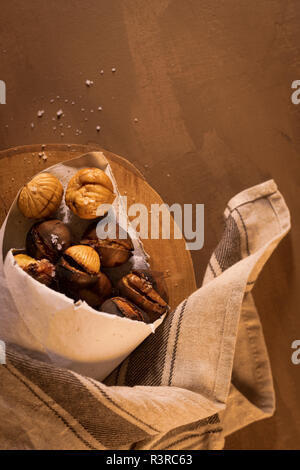 Gebratene Kastanien in einer Papiermembran, auf eine rustikale Küche Arbeitsplatte. Stockfoto