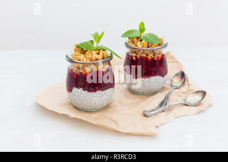 Zwei Gläser von Chia Pudding mit Kokosmilch, Rote Grütze und Erdnuss Müsli nachfüllen Stockfoto