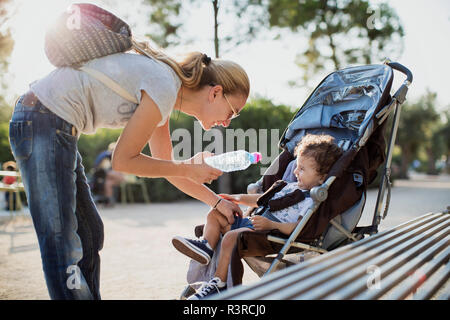 Mutter, die Wasserflasche zu seinem Sohn, sitzen in Pram Stockfoto