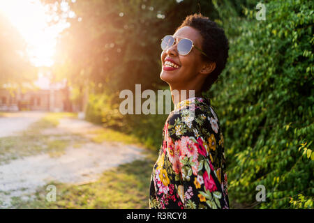 Glückliche junge Frau mit Sonnenbrille im Freien bei Sonnenuntergang Stockfoto