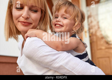 Lächelnde Mutter, die ihre Tochter piggyback vor ihrem Haus Stockfoto