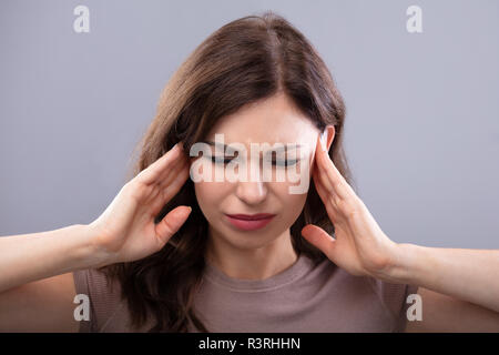 Junge Frau leidet unter Kopfschmerzen auf grauem Hintergrund Stockfoto
