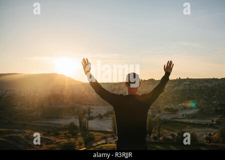 Ein Mann steht auf einem Berg in der Einsamkeit, bewundert die schöne Aussicht auf die natürliche Landschaft und hebt seine Hände bis zu zeigen, wie er frei und glücklich. Stockfoto