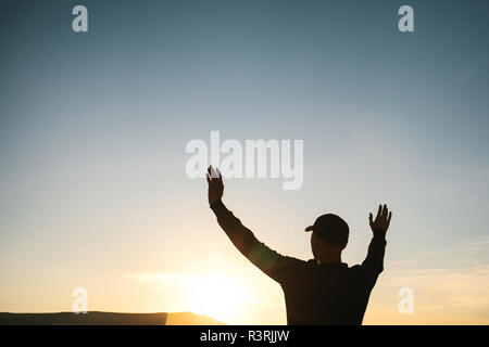 Ein Mann steht auf einem Berg in der Einsamkeit, bewundert die schöne Aussicht auf die natürliche Landschaft und hebt seine Hände bis zu zeigen, wie er frei und glücklich. Stockfoto