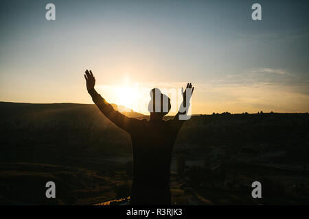 Ein Mann steht auf einem Berg in der Einsamkeit, bewundert die schöne Aussicht auf die natürliche Landschaft und hebt seine Hände bis zu zeigen, wie er frei und glücklich. Stockfoto