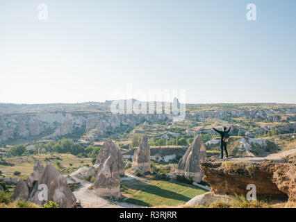Ein Mann steht auf einem Berg in der Einsamkeit, bewundert die schöne Aussicht auf die Naturlandschaft in Kappadokien in der Türkei und hebt seine Hände bis zu zeigen, wie er frei und glücklich. Stockfoto