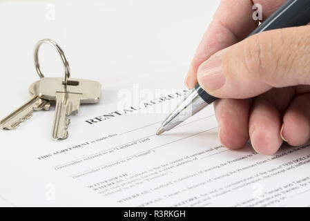 Hand ist das Schreiben mit einem Stift auf ein Mietvertrag Dokument, Hausschlüssel im Hintergrund, ausgewählte konzentrieren, enge Tiefenschärfe Stockfoto