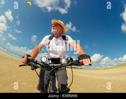 Frankreich, Bretagne, Sainte-Anne la Palud, Plage de Treguer, älterer Mann Riding Mountain e-Bike am Strand Stockfoto