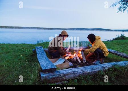Schweden, Lappland, zwei Freunde an einem Lagerfeuer am Seeufer Stockfoto