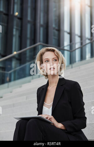 Portrait von blond Geschäftsfrau mit Tablet sitzen auf der Treppe im Freien Stockfoto