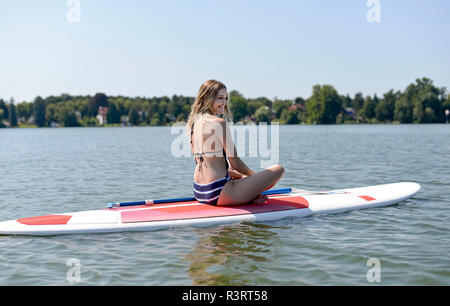 Deutschland, Brandenburg, glückliche junge Frau entspannend auf paddleboard auf Zeuthener Siehe Stockfoto