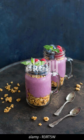 Zwei Gläser Joghurt mit Erdnuss Müsli, aronia Pulver und Nachfüllen von gehackten Haselnüssen und Gefrorene Beeren Stockfoto