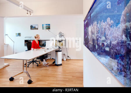 Junge Frau am Schreibtisch arbeiten im Büro mit einem Aquarium Stockfoto