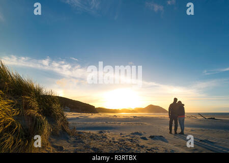 Neuseeland, Südinsel, Puponga, Wharariki Beach, Paar am Strand bei Sonnenuntergang Stockfoto