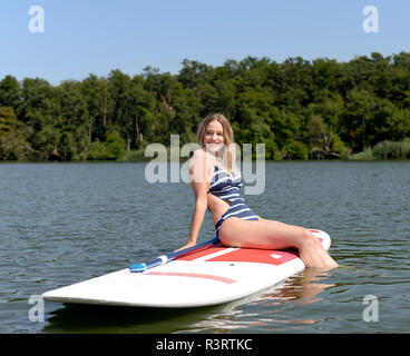 Deutschland, Brandenburg, Portrait von lächelnden jungen Frau entspannend auf paddleboard auf Zeuthener Siehe Stockfoto