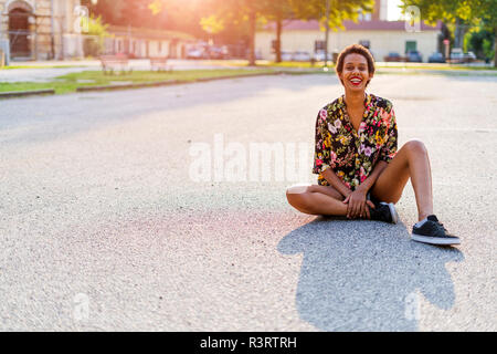 Portrait von Lachende junge Frau sitzt im Freien bei Sonnenuntergang Stockfoto