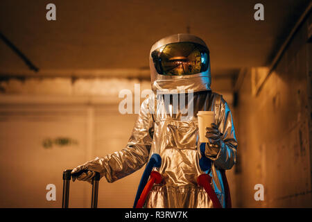 Spaceman in der Stadt in der Nacht stehend in Unterführung mit rollenden Koffer und Kaffee zum Mitnehmen Stockfoto