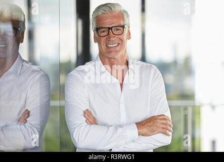 Unternehmer im Amt lehnte sich gegen Fenster, mit gekreuzten Armen Stockfoto