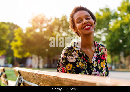 Portrait von lächelnden jungen Frau auf der Bank im Park